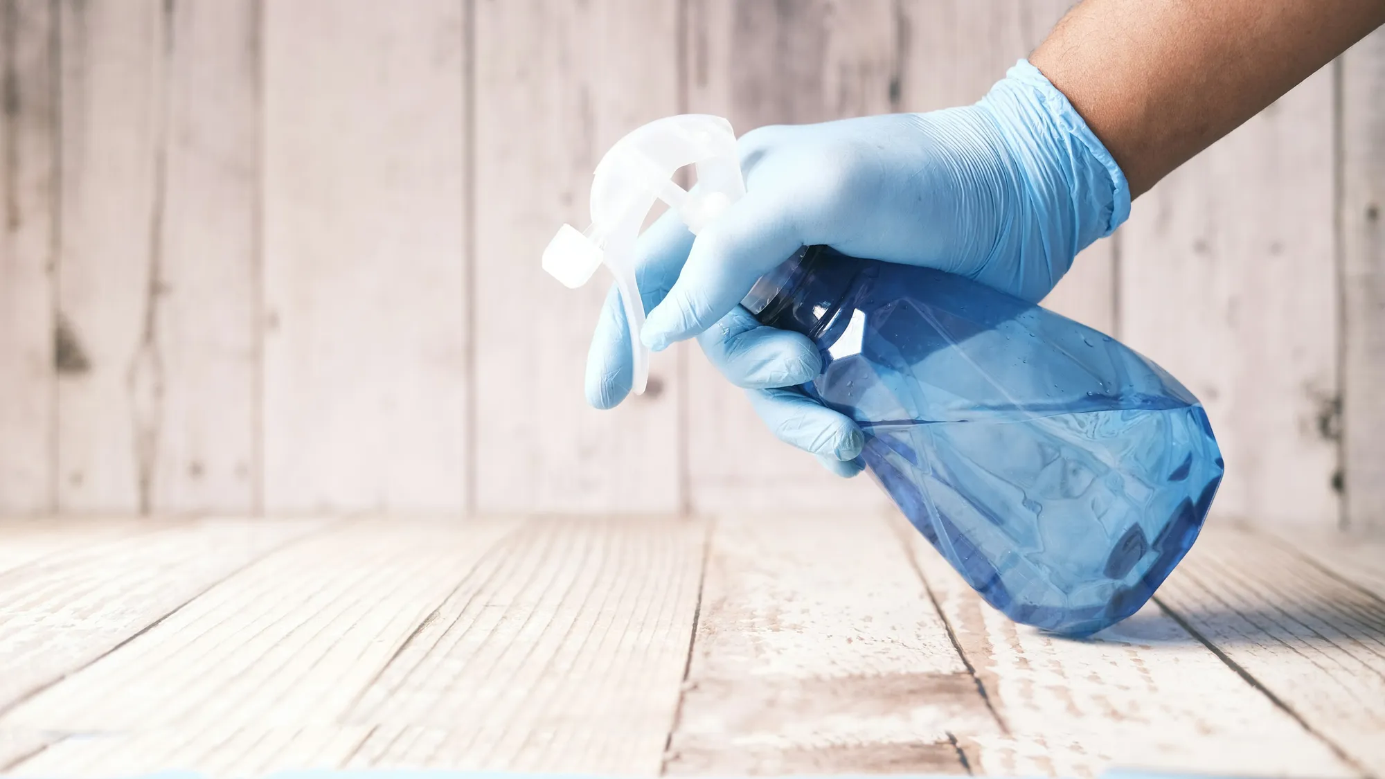 Gloved hand holding a spray bottle of cleaner